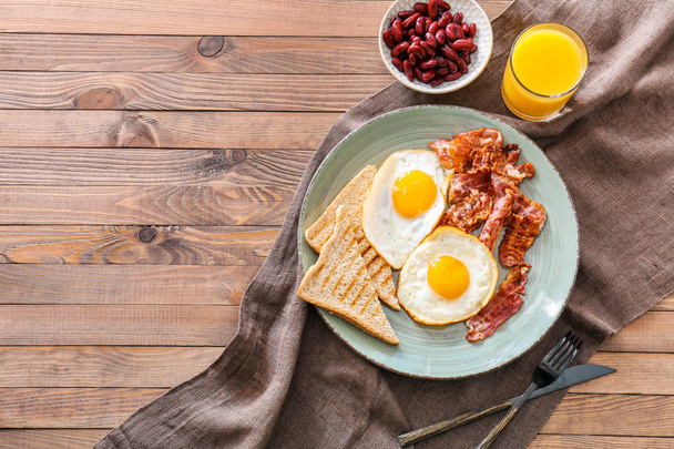 Вкусный английский завтрак с яичницей, беконом, бобами и тостами на столе
 - Фото, изображение