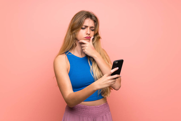 Nuori blondi nainen yli eristetty vaaleanpunainen tausta ajattelua ja lähettää viestin
 - Valokuva, kuva