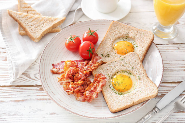 Talíř s chutnými smaženými vejci, slaninou, toastami a rajčaty na dřevěné pozadí - Fotografie, Obrázek