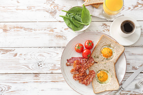 Placa con sabrosos huevos fritos, tocino, tostadas y tomate sobre fondo de madera
 - Foto, Imagen
