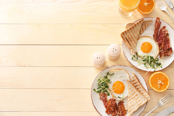 Тарелки с вкусными яичницами, беконом и тостами на столе
 - Фото, изображение