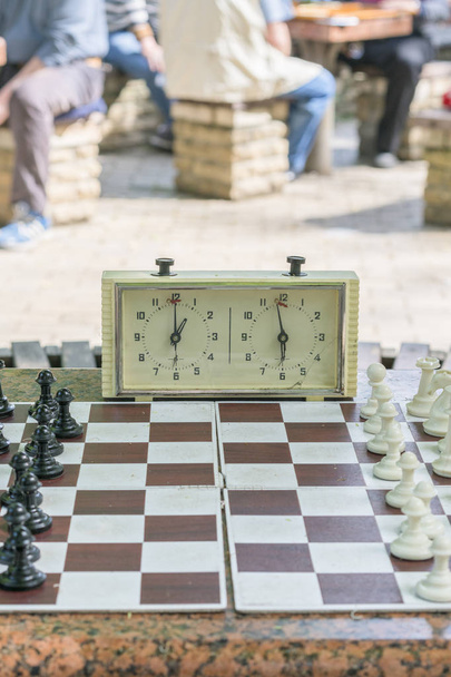 Šachová deska s kousky a hodinami na dřevěném stole v souvislosti s šachovým turnaji. Šachový turnaj s šachovým hodinami na dřevěném stole. vertikální fotografie - Fotografie, Obrázek