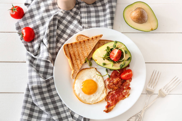 Plate with tasty fried egg, bacon, avocado and toasts on table - Photo, Image