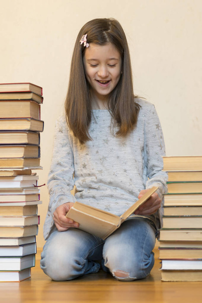 Dziewczyna czytając książkę siedzącą na podłodze w mieszkaniu. Cute Girl czytanie książki w domu. Edukacja i koncepcja szkoły-niewiele Uczeń dziewczyna siedzi na podłodze i czytania książki - Zdjęcie, obraz