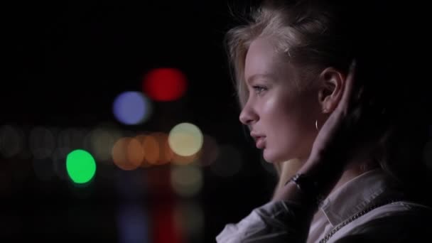 Beautiful blonde woman touch her long hair in night city - Materiał filmowy, wideo