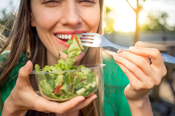 Όμορφη καυκάσιος γυναίκα τρώει σαλάτα πέρα από το πράσινο φυσικό υπόβαθρο - Φωτογραφία, εικόνα