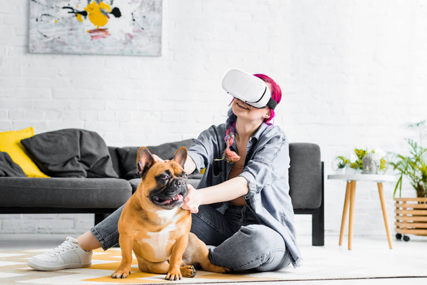 girl with colorful hair and VR headset sitting on floor and petting dog in cosy room - Foto, immagini