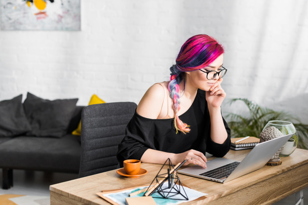 beautiful girl with colorful hair sitting behind table and using laptop in living room  - Photo, Image