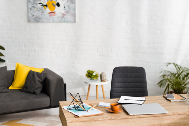 деревянный стол с ноутбуками, ноутбуком и чашкой кофе в гостиной с диваном
  - Фото, изображение