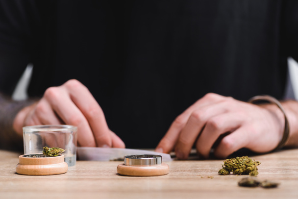 περικομμένη θέα του ανθρώπου που κάνει κοινή με την ιατρική μαριχουάνα ενώ κάθεται στο τραπέζι - Φωτογραφία, εικόνα