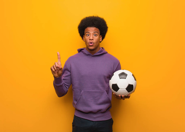 junger afrikanisch-amerikanischer Sportler, der einen Fußball in der Hand hält und eine großartige Idee, ein Konzept der Kreativität hat - Foto, Bild