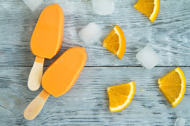 two yellow ice cream on a wooden background next to the sliced orange fruit and chopped ice. Concept summers food - Photo, Image