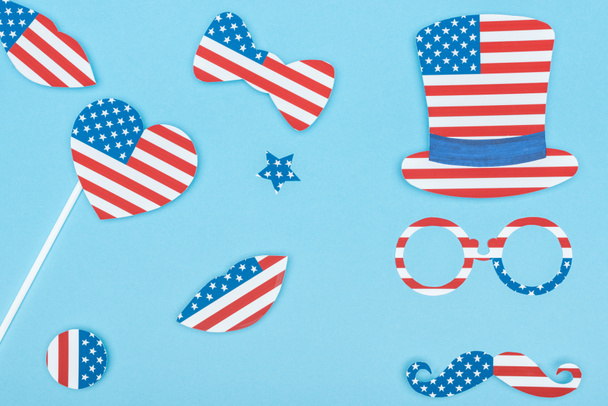 青い背景にアメリカの旗で作られた紙カット装飾口ひげ、眼鏡、帽子、唇とハートのトップビュー  - 写真・画像