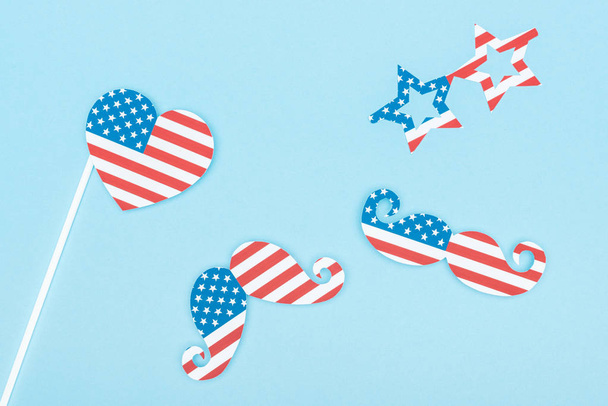 top view of paper cut decorative glasses, mustache and heart made of american flags on blue background - Foto, afbeelding