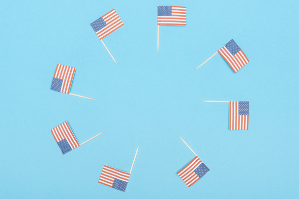 στρογγυλό πλαίσιο κατασκευασμένο από χαρτί κομμένα διακοσμητικά αμερικανικές σημαίες σε ξύλινα ραβδιά σε μπλε φόντο με χώρο αντιγραφής - Φωτογραφία, εικόνα