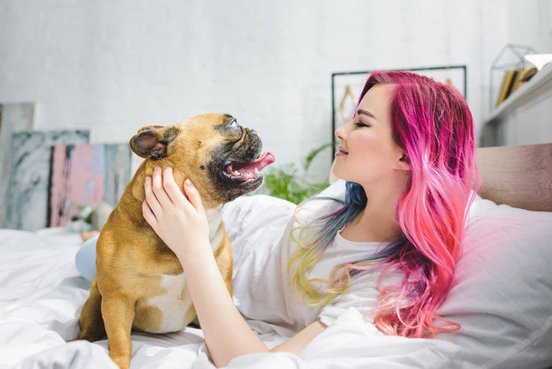 side view of attractive girl laying in bed and looking at french bulldog  - Photo, image