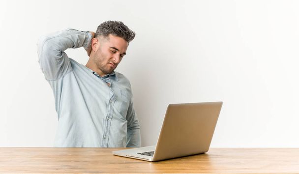Genç ve yakışıklı bir adam laptopuyla çalışıyor, kafasının arkasına dokunuyor, düşünüyor ve bir seçim yapıyor.. - Fotoğraf, Görsel