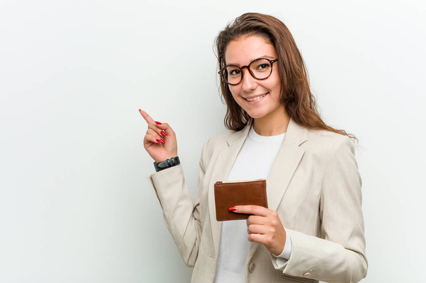 Genç Avrupalı iş kadını bir cüzdan tutuyor ve işaret parmağıyla işaret ederek gülümsüyor.. - Fotoğraf, Görsel