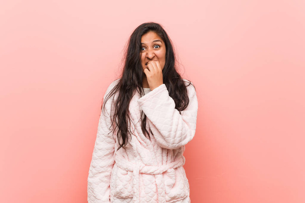 Young indian woman wearing pajama biting fingernails, nervous and very anxious. - Фото, изображение