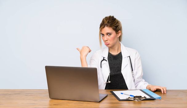 Blonde doctor woman unhappy and pointing to the side - Фото, изображение
