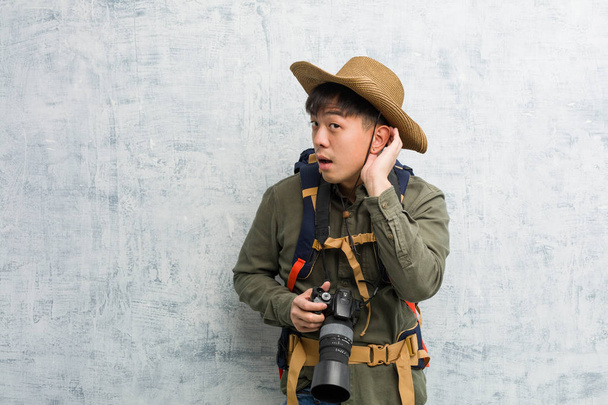 Young chinese explorer man holding a camera try to listening a gossip - Photo, Image