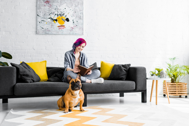 beautiful girl sitting on sofa in living room and small bulldog sitting on floor - Photo, Image