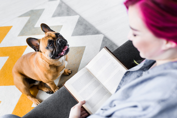 enfoque selectivo de la chica con colorido libro de lectura del pelo y bulldog francés sentado y mirando a la chica
 - Foto, imagen