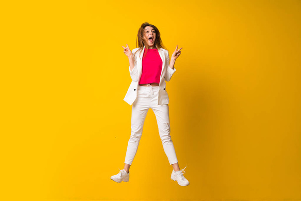 Young woman jumping over isolated yellow wall making victory ges - Photo, Image