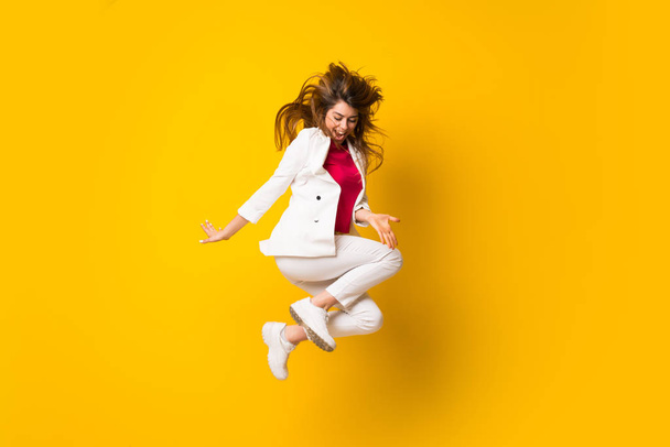 Young woman jumping over isolated yellow wall - Фото, зображення