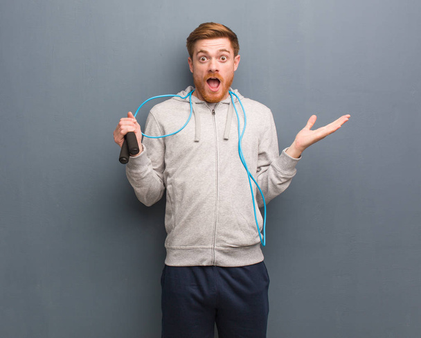Young redhead fitness man celebrating a victory or success. He is holding a jump rope. - Photo, Image