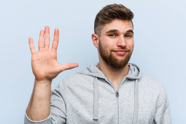 Young handsome fitness man smiling cheerful showing number five with fingers. - Photo, Image