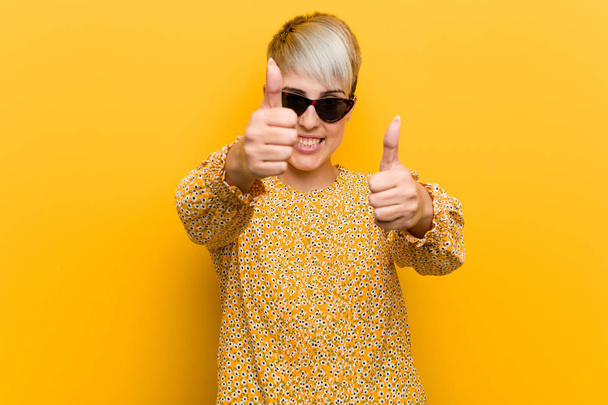 Young curvy woman wearing a floral summer clothes with thumbs ups, cheers about something, support and respect concept. - Photo, Image