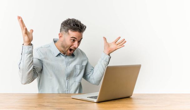 Mladý pohledný muž pracující se svým laptopem slaví vítězství nebo úspěch, je překvapen a šokován. - Fotografie, Obrázek