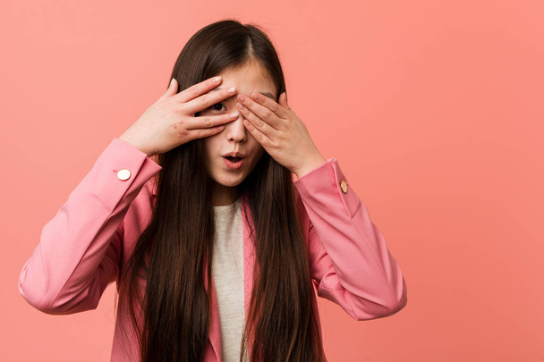 Fiatal üzleti kínai nő rózsaszín öltönyt visel pislogás ujjain keresztül rémült és ideges. - Fotó, kép