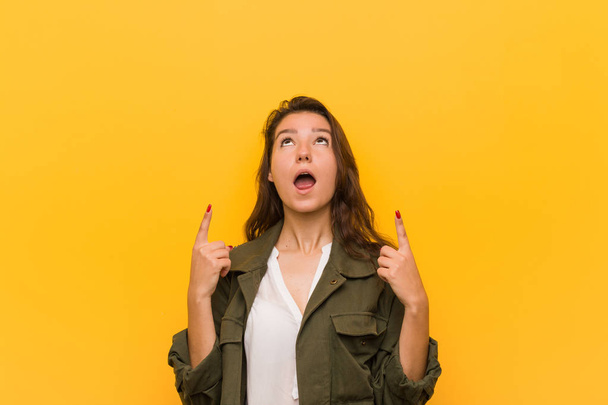 Nuori eurooppalainen nainen eristetty keltaisella pohjalla osoittaa ylöspäin suu auki
. - Valokuva, kuva