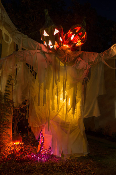 A scary display of a two headed pumpkin ghost at night with yellow lighting that adds to this halloween looking display - Photo, Image