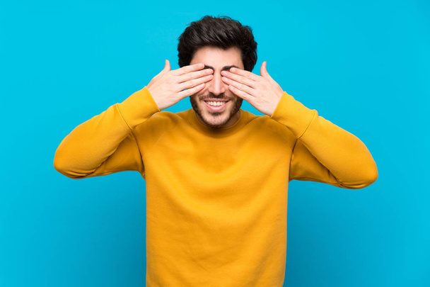 Handsome over isolated blue wall covering eyes by hands - Foto, afbeelding