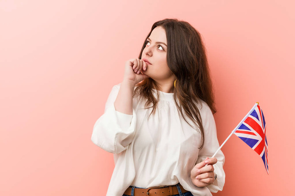 Young plus size curvy woman holding a united kingdom flag looking sideways with doubtful and skeptical expression. - Valokuva, kuva