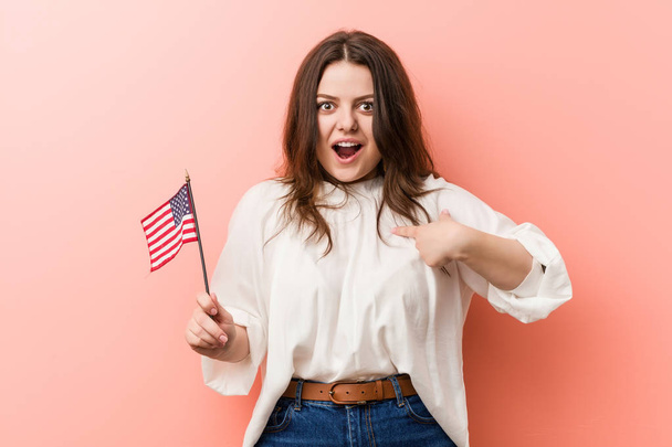 アメリカ国旗を手にした若いカービィプラスサイズの女性が驚いたことに自分自身を指差すと. - 写真・画像