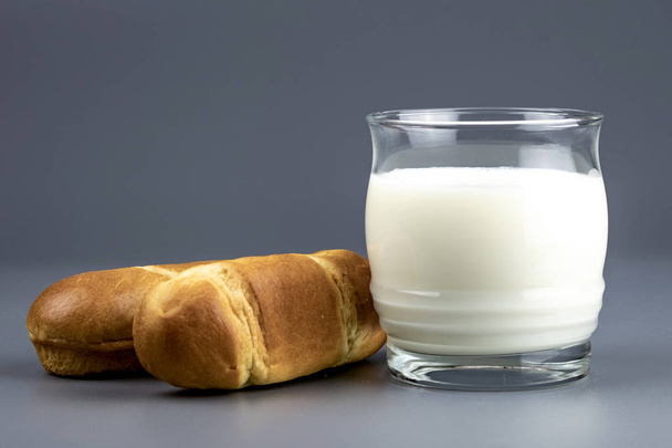 δύο ψωμάκια δίπλα σε ένα ποτήρι γάλα σε γκρι - Φωτογραφία, εικόνα