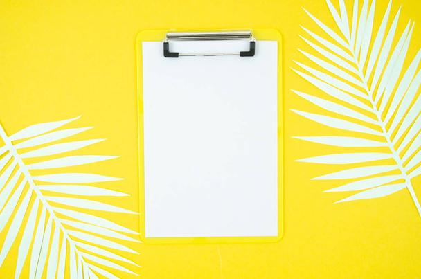 Sommerklemmbrett-Attrappe von oben mit leerer a4 Papierliste und Palmblatt auf gelbem Hintergrund. Wohnung lag mit Kopierraum - Foto, Bild