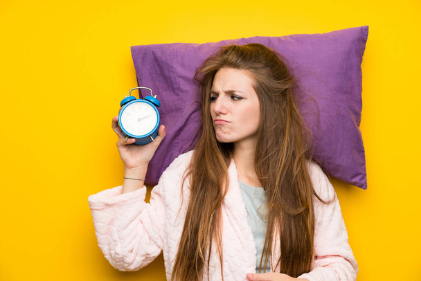 Jeune femme en robe de chambre dans un lit stressé tenant horloge vintage
 - Photo, image