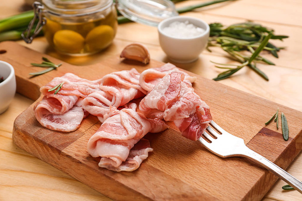 Fresh raw bacon and fork on wooden board - Фото, изображение