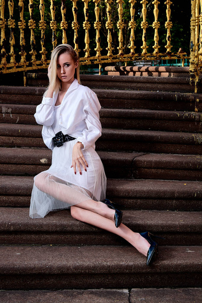 Blonde woman sits on the steps of the old granite stair. Young woman modern portrait. - Foto, imagen