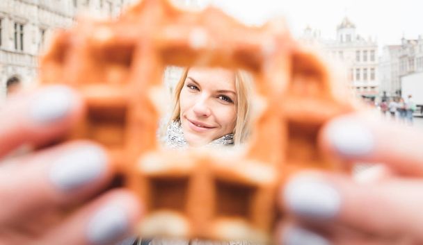 Woman holding a waffle against the backdrop of the Grand Place in Brussels, Belgium - Photo, Image