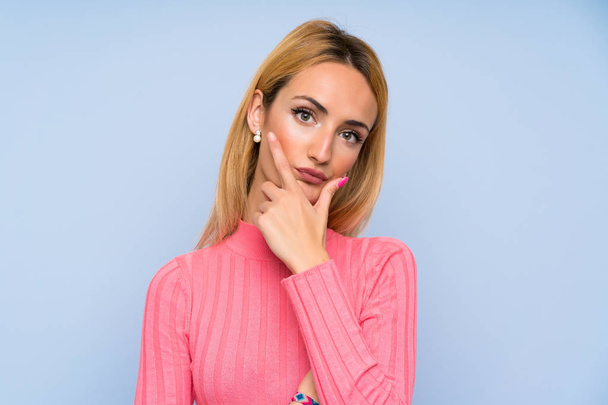 Jonge blonde vrouw met roze trui over geïsoleerde blauwe achtergrond staande en denken een idee - Foto, afbeelding
