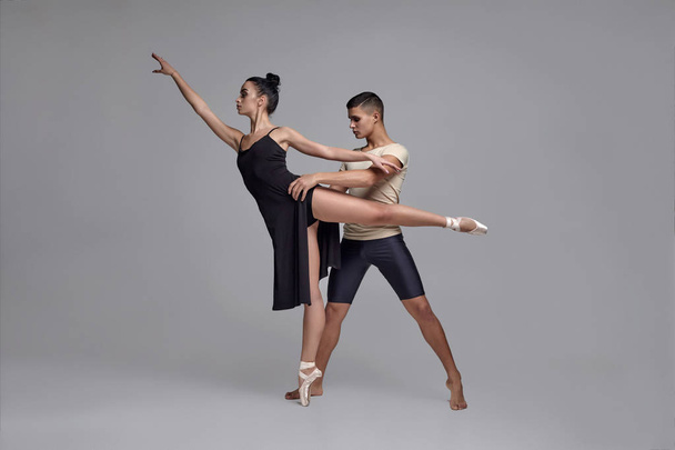 Δύο αθλητικές μοντέρνες χορεύτριες ποζάρουν σε ένα γκρίζο φόντο στούντιο. - Φωτογραφία, εικόνα