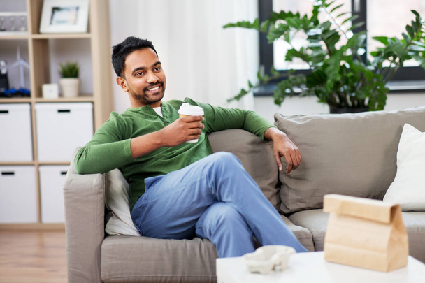 happy indian man drinking takeaway coffee at home - Photo, image