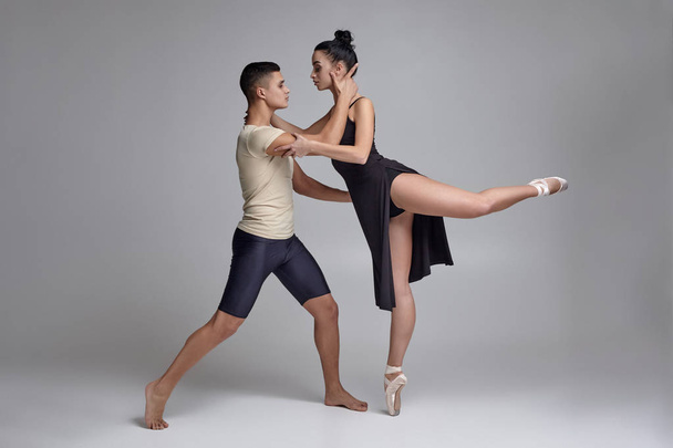 Twee atletische moderne balletdansers poseren tegen een grijze studio achtergrond. - Foto, afbeelding