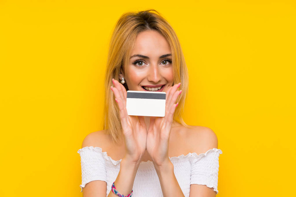Jeune femme blonde sur mur jaune isolé tenant une carte de crédit
 - Photo, image